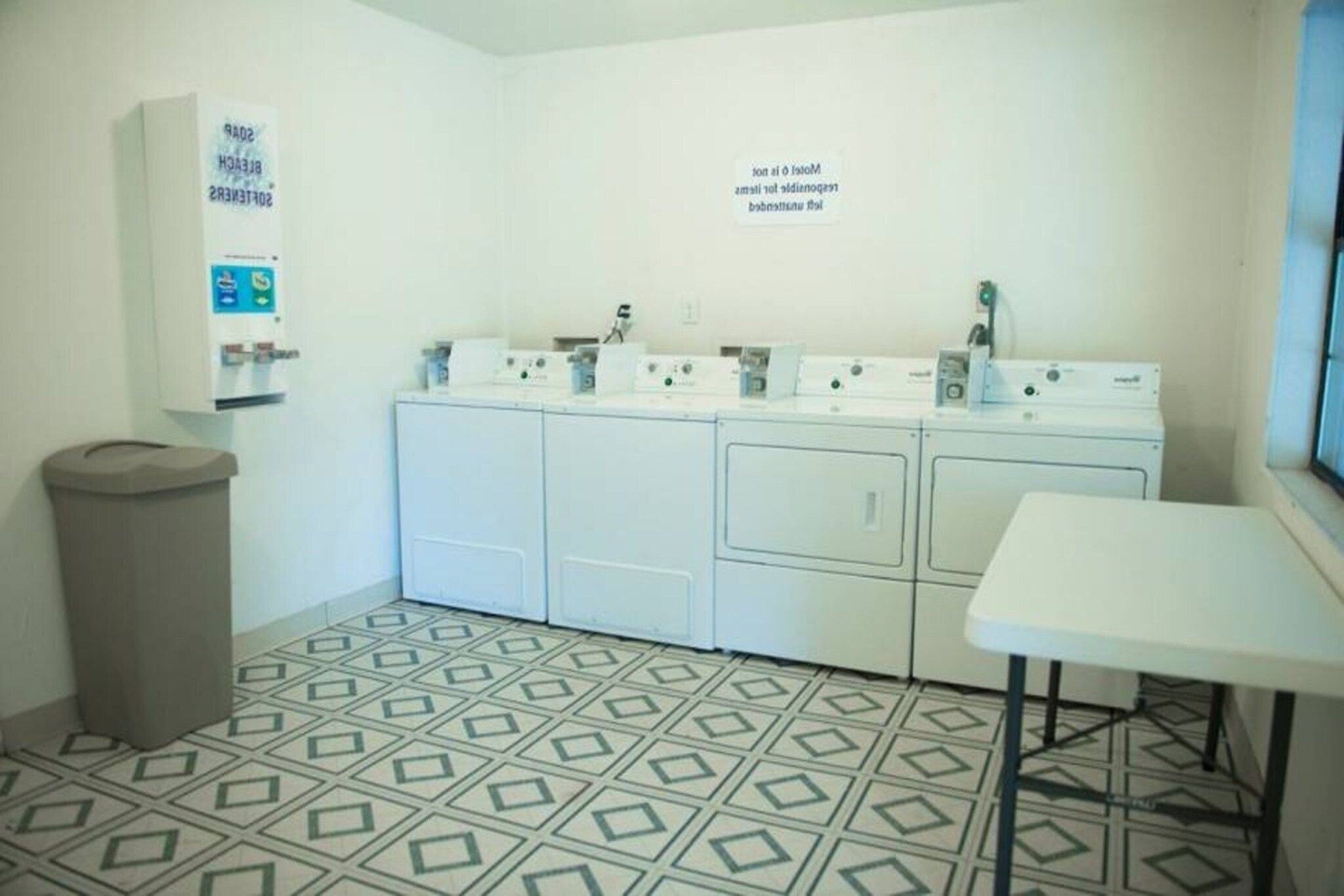 A laundry room with multiple washing machines, a trash bin, and a table.