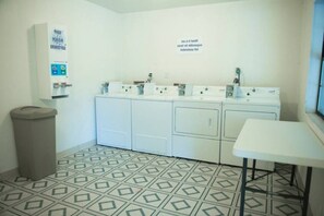 Une buanderie équipée de plusieurs machines à laver, d’une poubelle et d’une table.