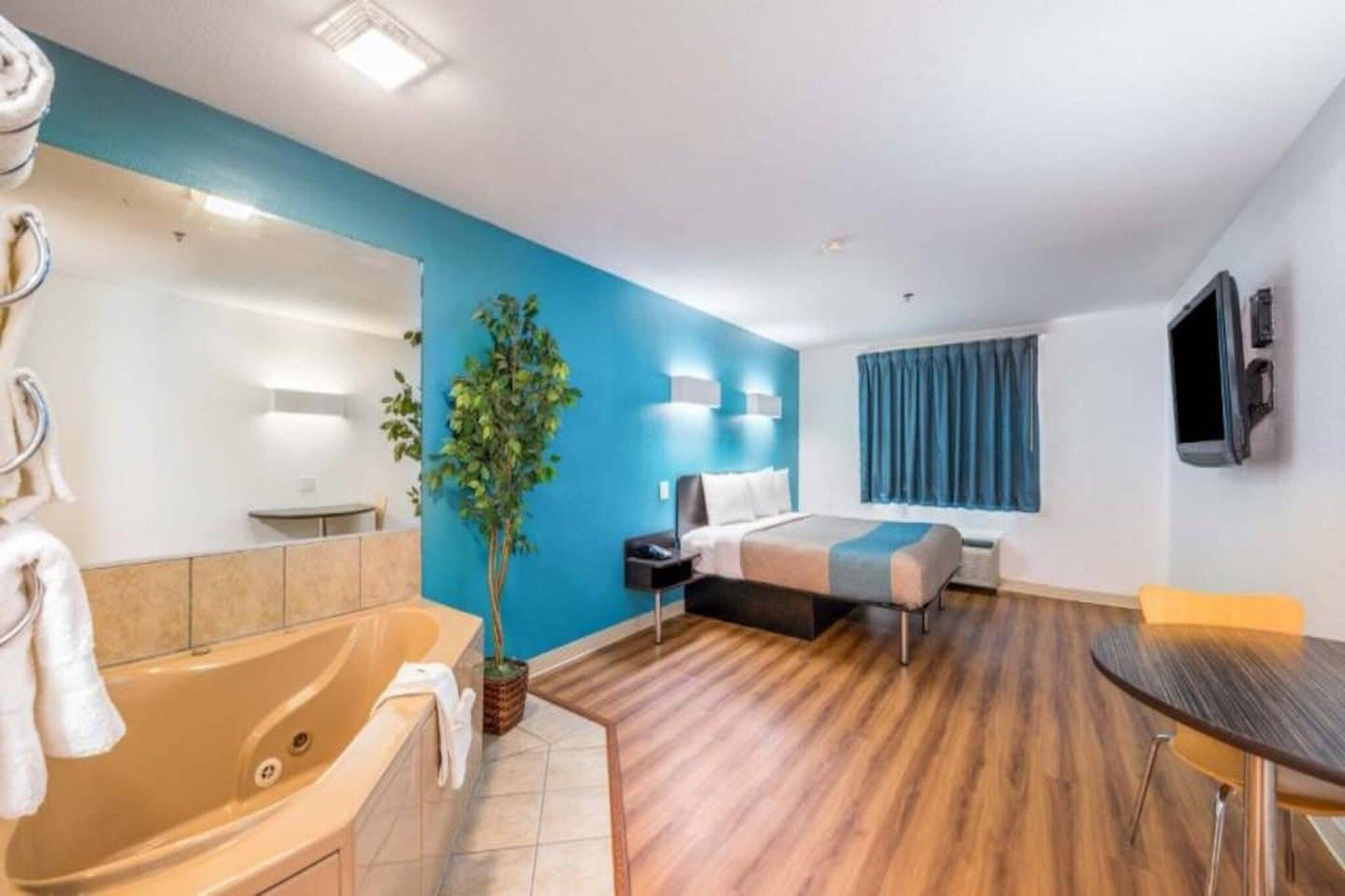 A modern hotel room with a bathtub, a bed, a dining table, and a large mirror.
