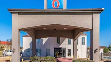 Een motel met een groot bord waarop een '6' staat, een overdekte ingang en een parkeerplaats.