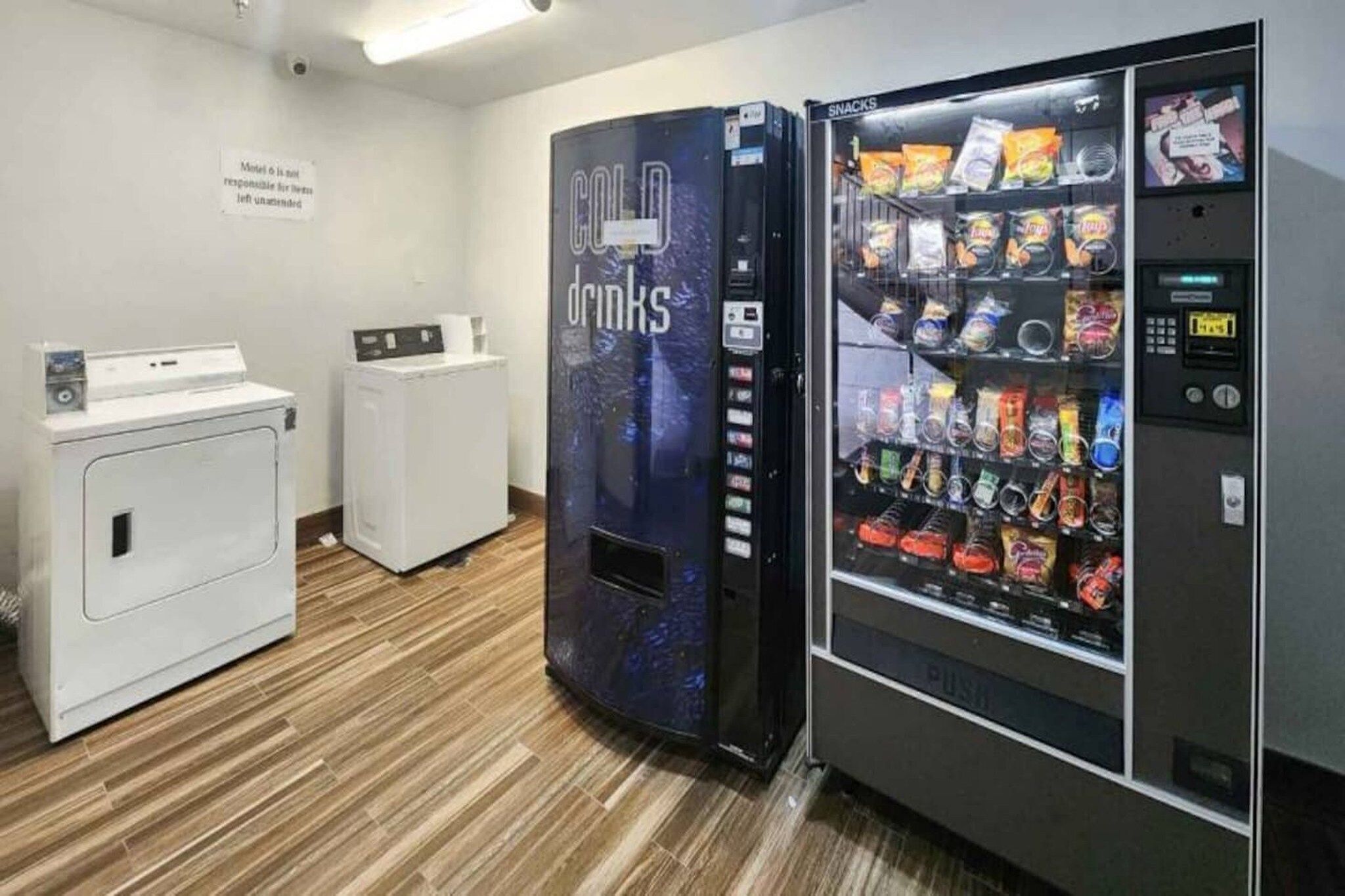 Une chambre d’hôtel équipée d’un distributeur automatique indiquant « BOISSONS FRAÎCHES » et d’un rayon « EN-CAS », ainsi que d’un lave-linge et d’un sèche-linge.