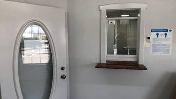 Una puerta con un panel de vidrio esmerilado, un ventanal pequeño con un estante y un aviso de seguridad en la pared.