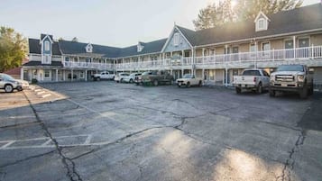 A motel with a parking lot, multiple vehicles, and a building with a balcony.