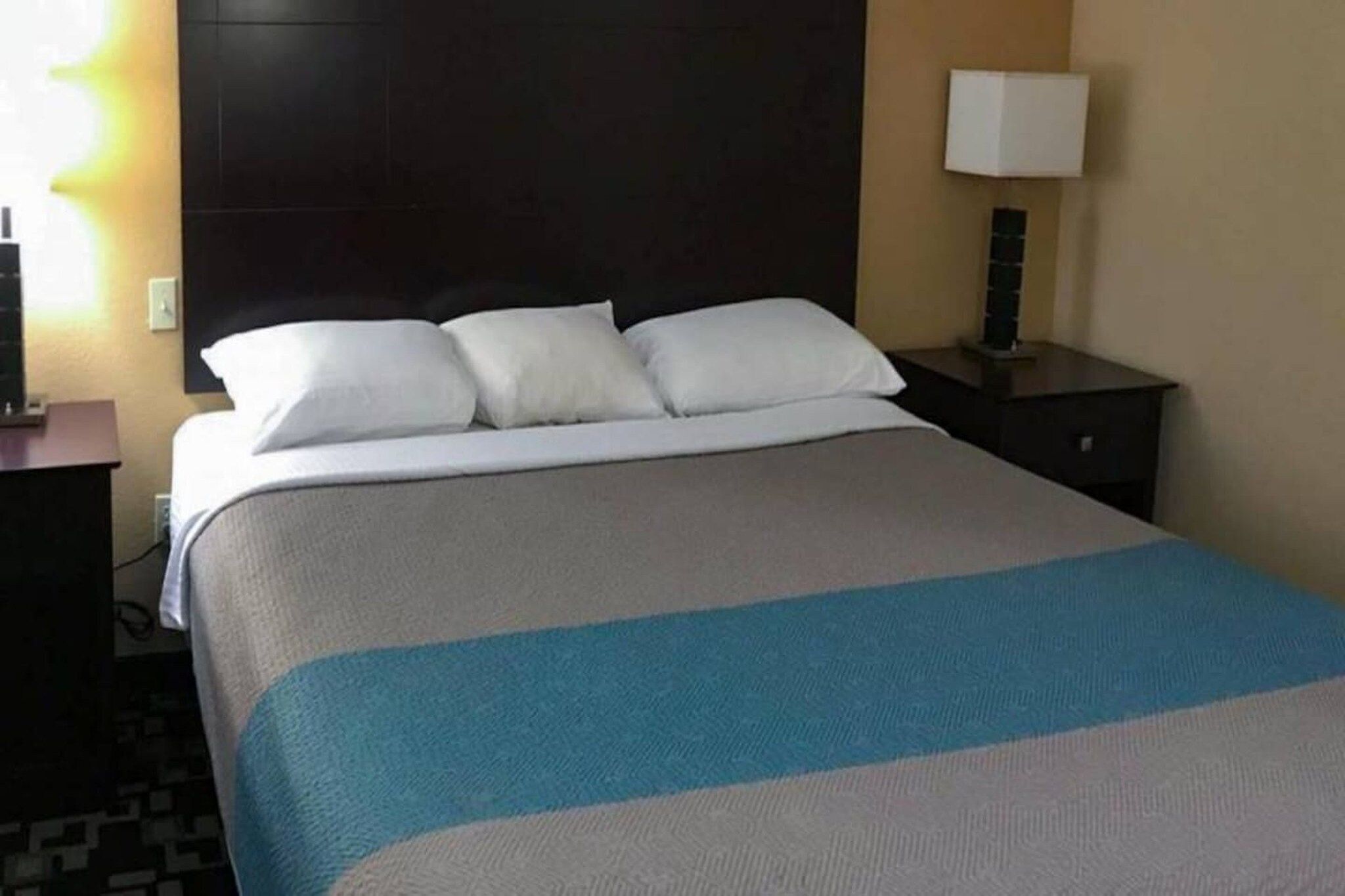 A hotel room with a bed, a nightstand, a lamp, and a wall-mounted light.