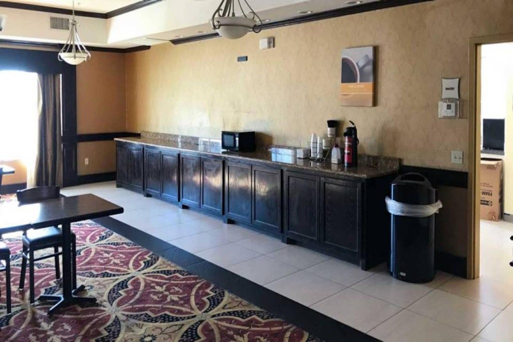 Quarto de hotel com cozinha equipada, com armários escuros, micro-ondas e máquina de café no balcão.