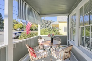 A covered porch with wicker furniture, a table with a vase, and a view of the street and houses. - McCloud Retreat Near Mt Shasta & Waterfalls! (McCloud)