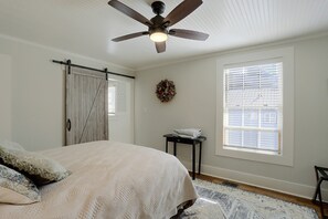A bedroom with a bed, a ceiling fan, a window with blinds, a door, and a small table with towels. - McCloud Retreat Near Mt Shasta & Waterfalls! (McCloud)