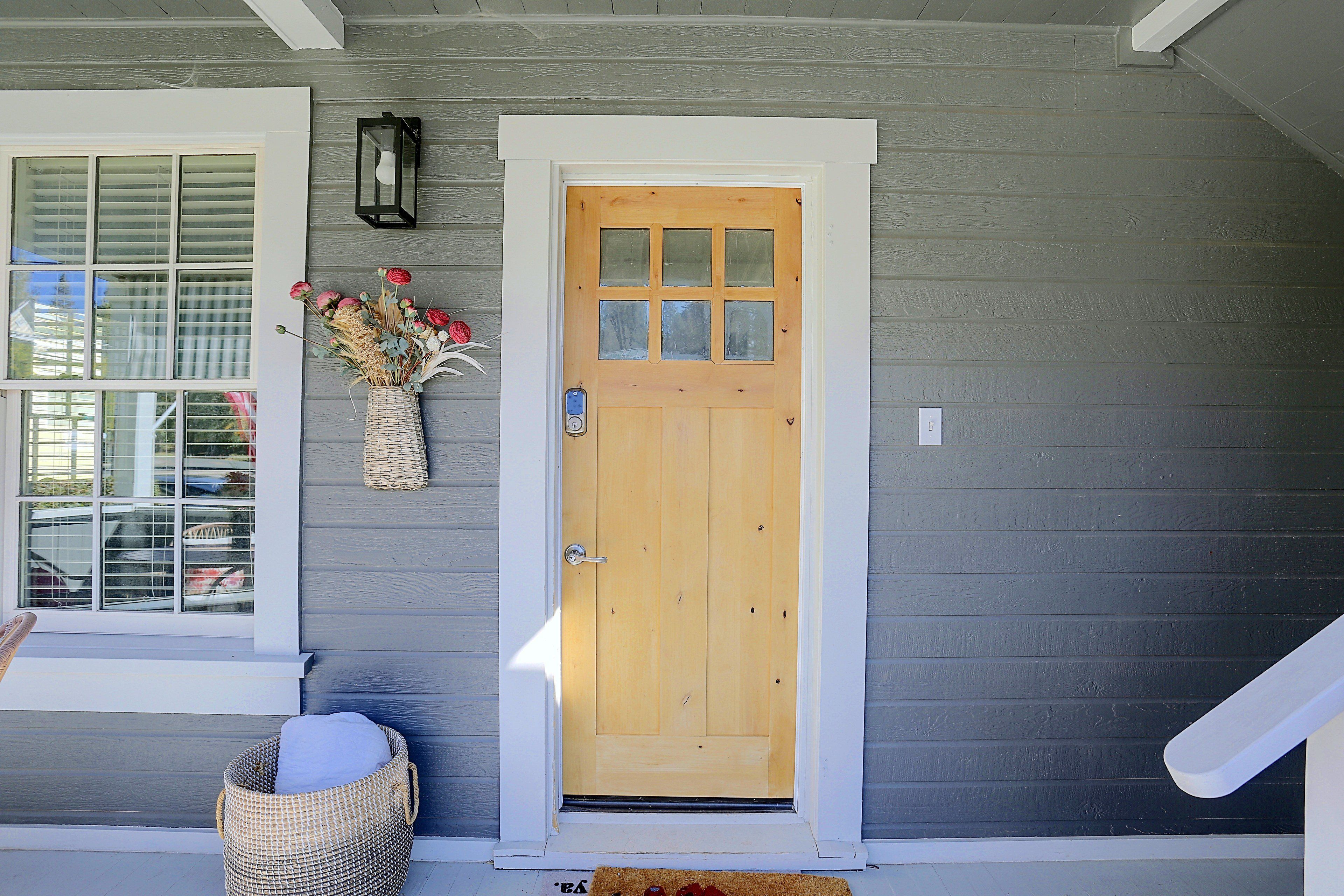 A wooden front door with a glass panel, a white-framed window, and a basket with a cushion on the porch.