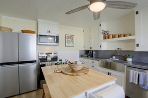 Une cuisine moderne dotée d’appareils électroménagers en acier inoxydable, de plans de travail en bois et d’un ventilateur de plafond.