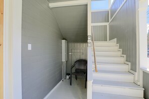 Un escalier étroit menant à une porte, avec une chaise et un coffret électrique adossés au mur.