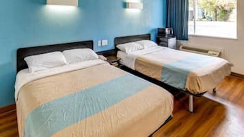A hotel room with two beds, a desk, a chair, a window with curtains, and a wall-mounted heater.