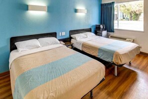 A hotel room with two beds, a desk, a chair, a window with curtains, and a wall-mounted heater. - 2 Queen Beds | Smoking (Waco)