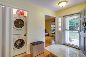 A laundry room with two stacked washing machines, a small utility cart, and a door leading to a living area with a view of the outdoors. - 1 Mi to Colonial Beach! Coastal Escape w/ Fire Pit (Colonial Beach)