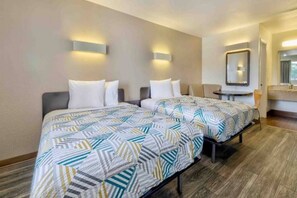 A hotel room with two beds, a small table, a mirror, and a bathroom.