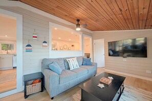 A modern living room with a grey sofa, a black coffee table, and a television mounted on the wall. - Big Alum Pond Escape w/ Dock & Fire Pit! (Sturbridge)