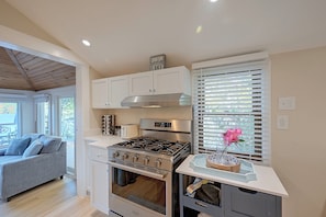 A modern kitchen with white cabinetry, a stainless steel stove, and a window with blinds. - Big Alum Pond Escape w/ Dock & Fire Pit! (Sturbridge)