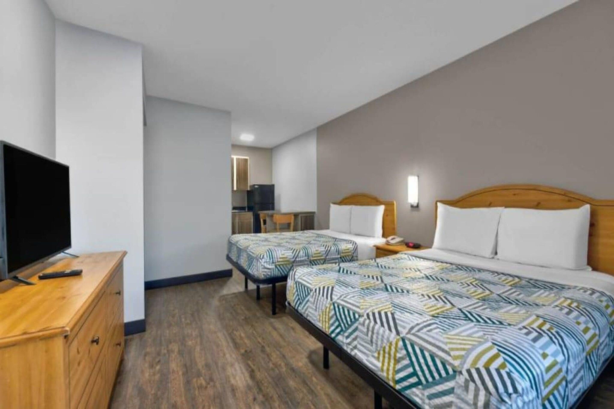 A hotel room with two beds, a television, a desk, and a small kitchenette.