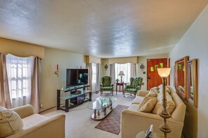 A living room with a television, two green armchairs, a sofa, a glass coffee table, and a lamp. - 1 Mi to Notre Dame & Dtwn: Charming Home w/ Yard (South Bend)