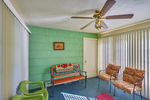 A room with a ceiling fan, a bench with a decorative headboard, two patterned chairs, a door, and a window with vertical blinds. - 1 Mi to Notre Dame & Dtwn: Charming Home w/ Yard (South Bend)