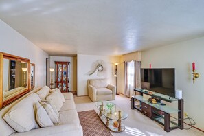 A living room with a sofa, a television, a glass coffee table, and a decorative wall piece. - 1 Mi to Notre Dame & Dtwn: Charming Home w/ Yard (South Bend)