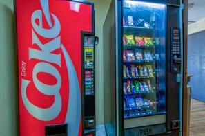 A Coca-Cola vending machine and a beverage dispenser with various drinks and snacks. - Spacious 1 KING BED | NON-SMOKING (ARLINGTON)