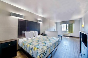 A modern hotel room with a large bed, bedside tables, a TV, and a window with curtains. - Spacious 1 KING BED | NON-SMOKING (ARLINGTON)