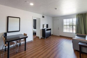 A room with a wooden floor, a dining table with chairs, a sofa, a TV stand, and a window with curtains. - 2 Full Beds |Suite,Nsmk,Kitchen (Arlington)