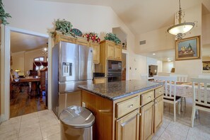 A kitchen with a stainless steel refrigerator, wooden cabinets, a granite countertop, and a dining area with a white table and chairs. - Patio & Grill! Spacious Las Vegas Oasis (Las Vegas)