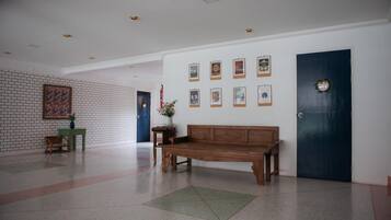 A lobby with a wooden bench, a wall with framed pictures, a blue door, and a brick wall with a painting.
