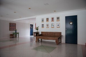 A lobby with a wooden bench, a wall with framed pictures, a blue door, and a brick wall with a painting.