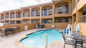 A hotel with a swimming pool, outdoor seating, and multiple balconies.