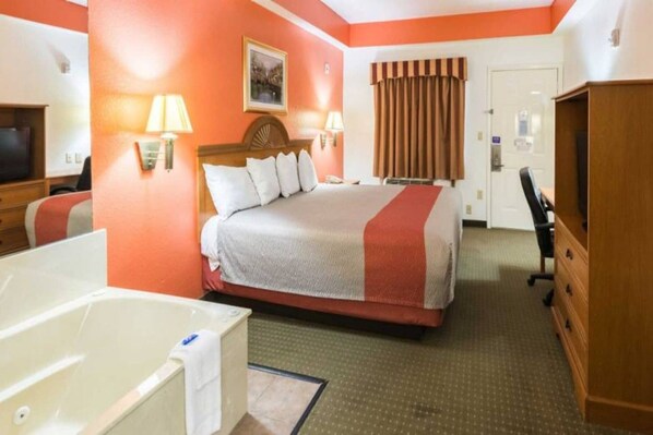 Quarto de hotel com cama, escrivaninha, cadeira, televisão e banheira.