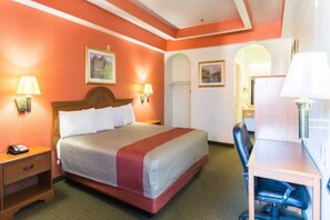 Una habitación de hotel con una cama, lámparas de noche, un escritorio y una silla.
