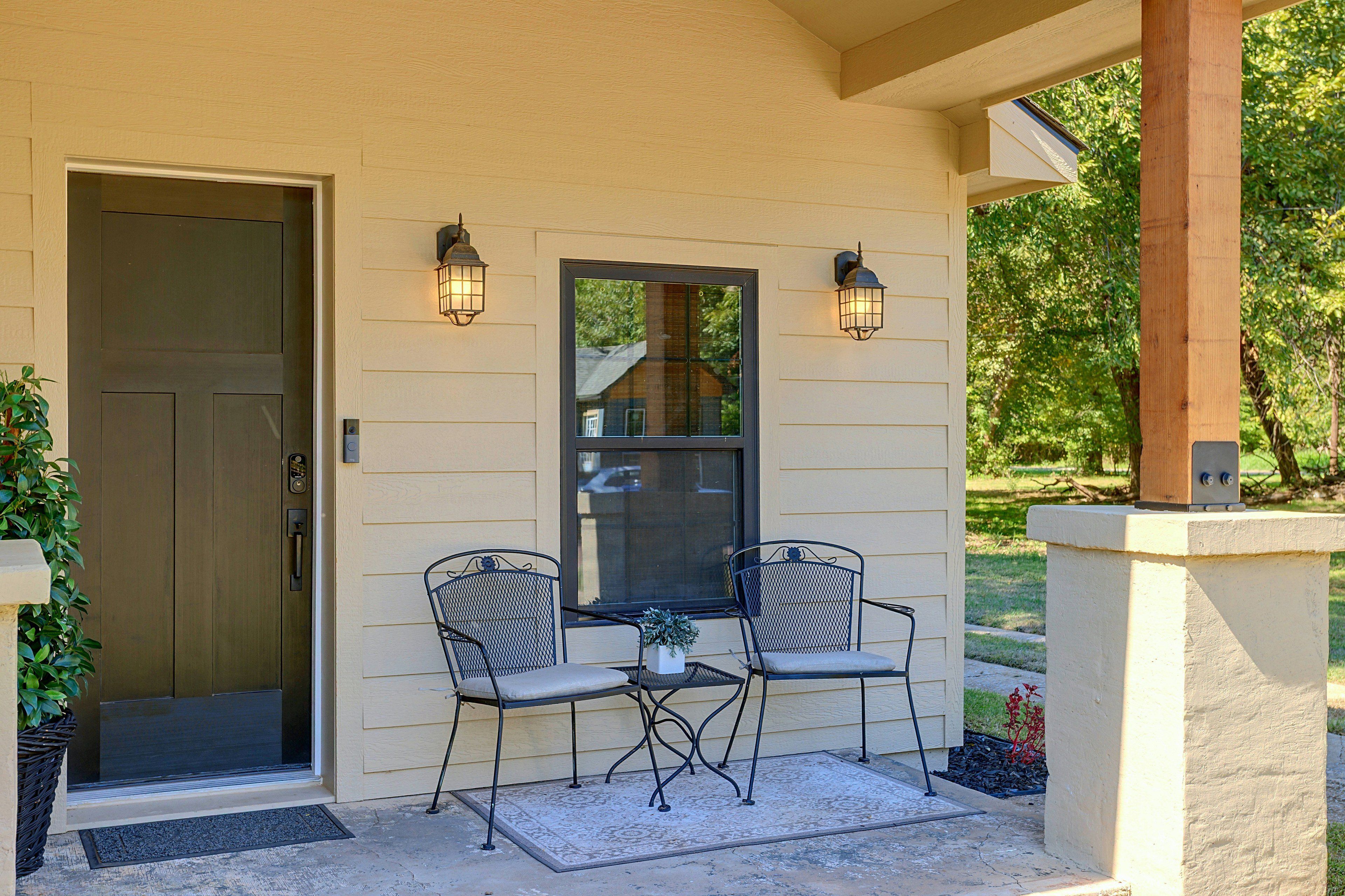 A covered porch with a door, two chairs, a table, and two wall-mounted lights.