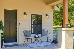 A covered porch with a door, two chairs, a table, and two wall-mounted lights. - Guthrie Home in the Heart of Historic Downtown! (Guthrie)