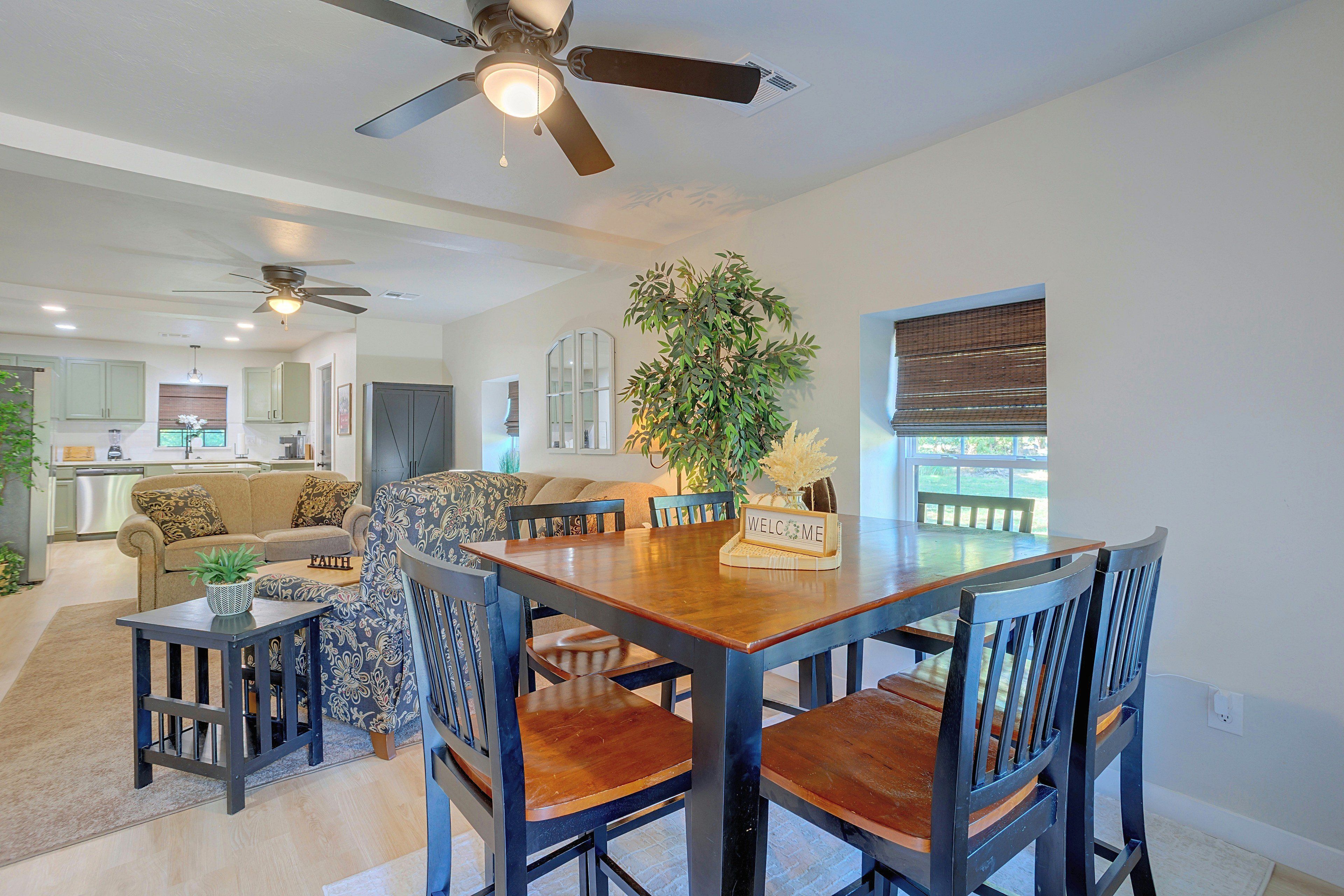 A dining area with a wooden table and chairs, a ceiling fan, and a view of the kitchen in the background.