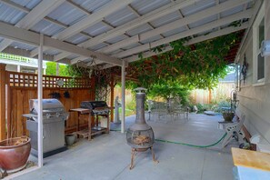 Eine überdachte Terrasse mit Grill, Gartenmöbeln und einem dekorativen Metallschornstein.