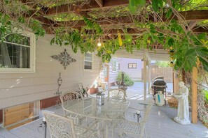 Une terrasse extérieure avec une table et des chaises en verre, entourée de verdure et agrémentée d’une pergola.