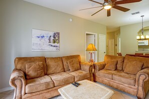 A living room with a brown leather sofa, a coffee table, and a ceiling fan. - Resort Perks! Family Condo 4 Mi to Disney World! (Kissimmee)