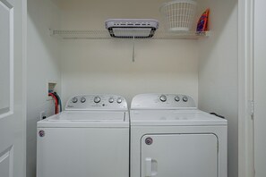 Een wasserette met twee witte Whirlpool wasmachines en drogers, een witte dakventilatie en een wasmand op een plank.