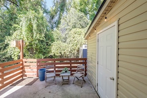 A patio with a wooden fence, a table, two chairs, a potted plant, and a blue trash can. - 6 Mi to the Masters: North Augusta Condo (North Augusta)