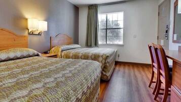 A hotel room with two beds, a desk, a chair, a window with curtains, and a lamp.