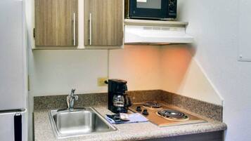 A compact kitchenette with a stainless steel sink, a coffee maker, a microwave, and a gas stove.