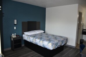 A single bed with a patterned bedspread, a bedside table with a phone, and a wall-mounted light fixture. - 1 Full Bed | Non-Smoking, Kitchen (Grand Prairie)