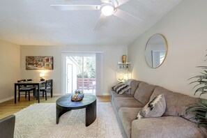 Un salon comprenant un canapé, une table basse, un coin repas avec des chaises, un tableau et un ventilateur de plafond.