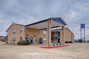 A motel with a covered parking area, multiple rooms, and a visible sign indicating the establishment number.