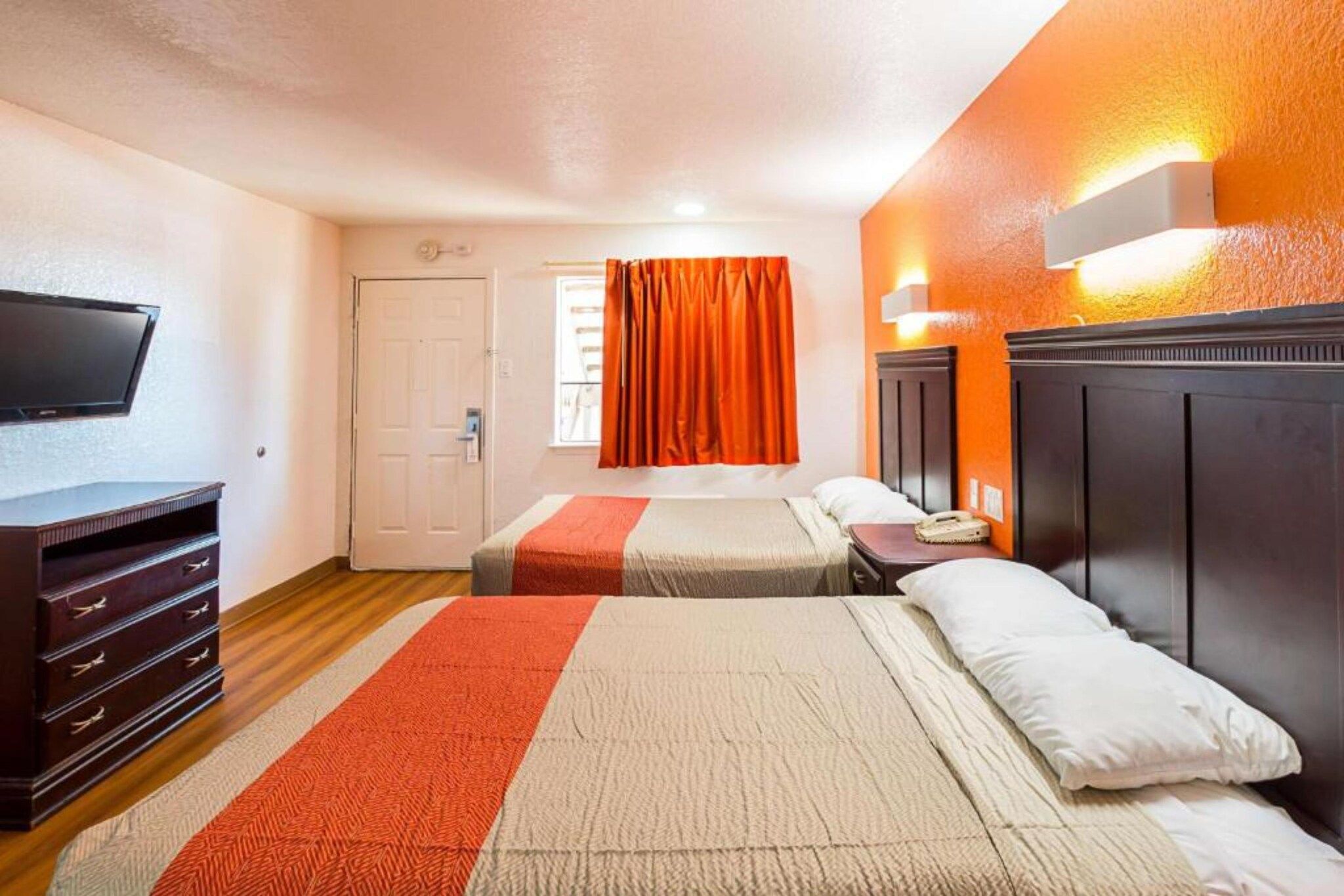 A hotel room with two beds, a television, a dresser, and a window with curtains.