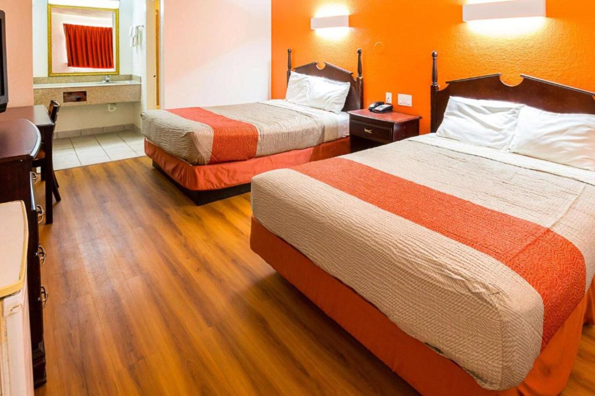 Een hotelkamer met twee bedden, houten vloeren, een bureau en een spiegel.
