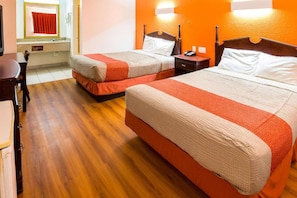 A hotel room with two beds, wooden flooring, a desk, and a mirror.