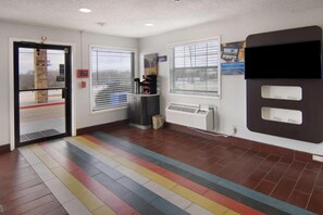 Un hall d’hôtel avec un sol carrelé, un comptoir d’accueil et un grand meuble mural noir doté d’un écran.